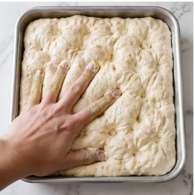 Step 3: Dimple the proofed dough with buttered fingertips before baking.