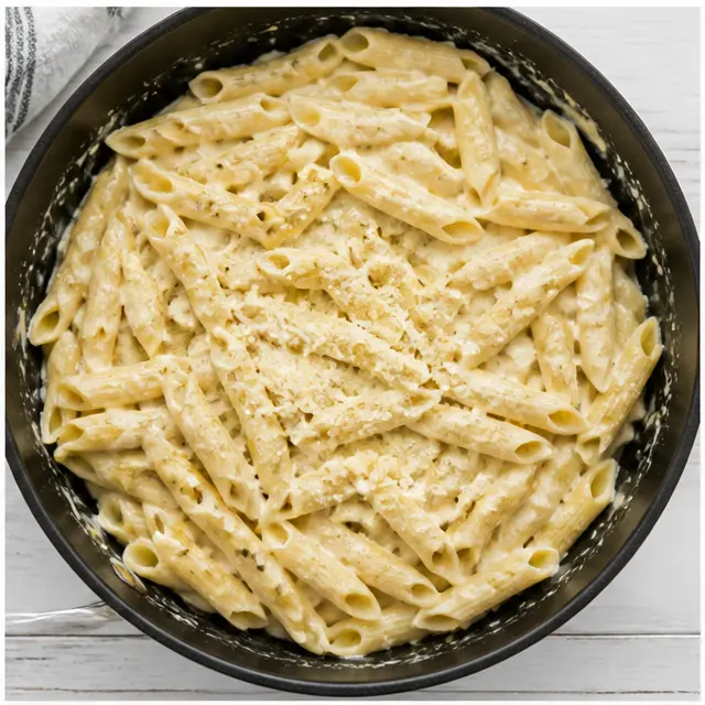 Tossing cooked penne into the glossy parmesan cream sauce