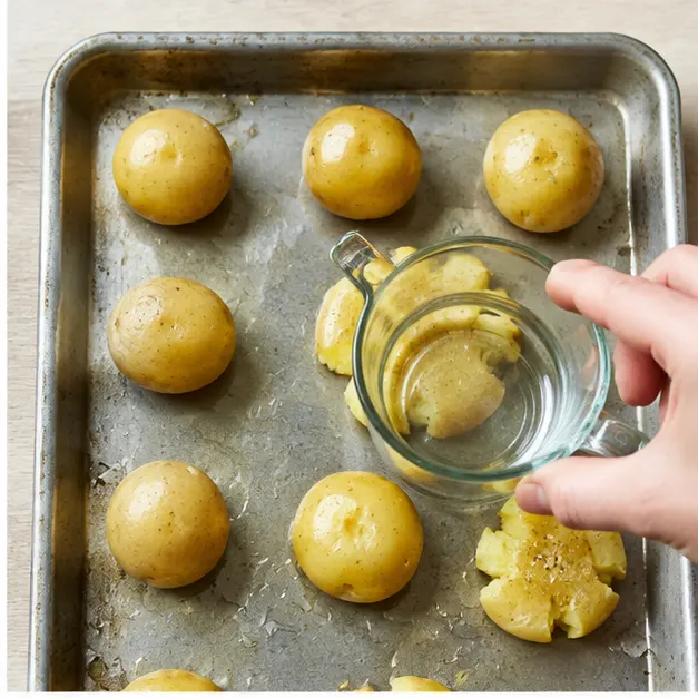 Step 2: Smashing boiled potatoes flat with a measuring cup on an oiled sheet pan