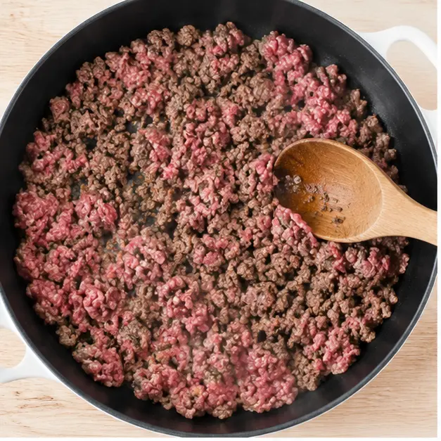 Browning ground beef in skillet with wooden spoon