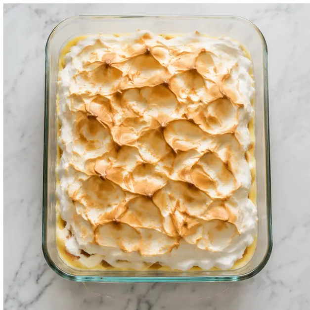 Baking the assembled pudding until the meringue topping turns golden brown